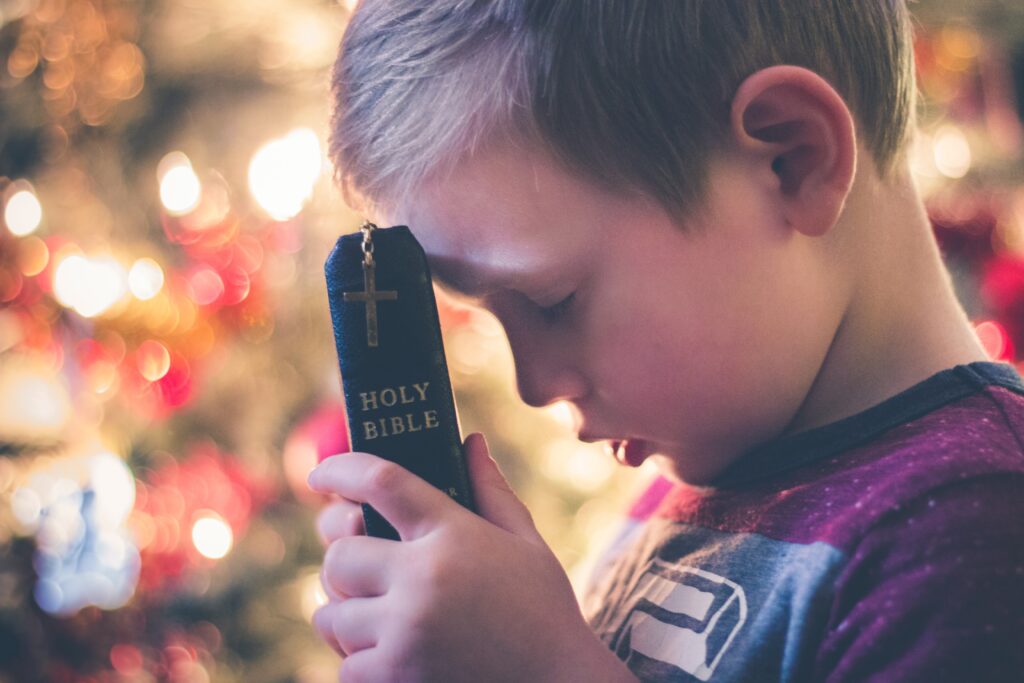 Child praying with a Bible in hand